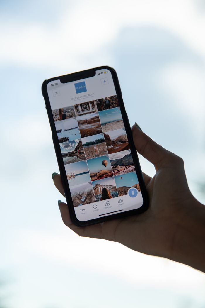 A smartphone in hand showing a gallery of travel photos against a clear sky.